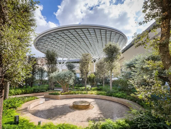 Street-level view of ABC Verdun Mall in Beirut showing the modern multi-story façade with glass panels, open terraces, and people walking along the ground-level shops and shaded walkways.