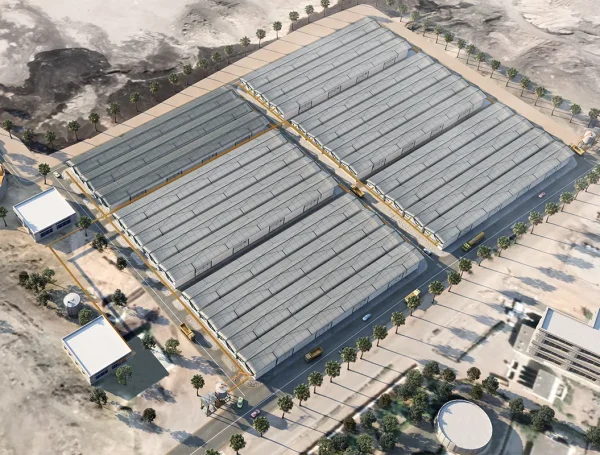 Aerial view of a large industrial or logistics facility with multiple long warehouse buildings, surrounded by roads, palm trees, and support infrastructure in a desert environment.