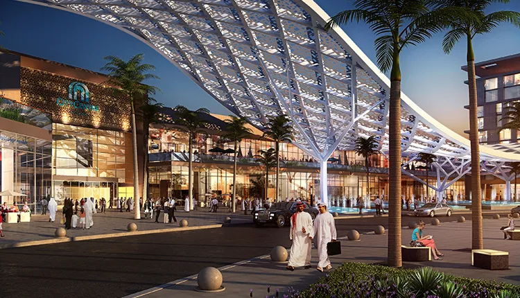 Evening scene at an upscale shopping mall entrance with a large illuminated canopy, palm trees, fountains, and people walking, including two men in traditional Middle Eastern attire.