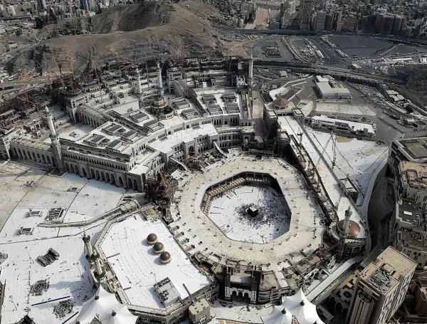 Aerial view of Masjid al-Haram in Mecca, Saudi Arabia, showing the Kaaba at the center surrounded by the mosque's white marble courtyard and ongoing construction.