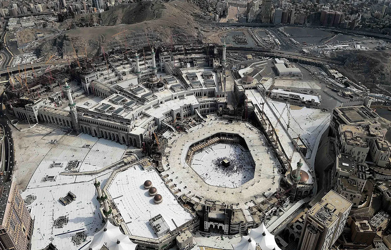 Aerial view of Masjid al-Haram in Mecca, Saudi Arabia, showing the Kaaba at the center surrounded by the mosque's white marble courtyard and ongoing construction.